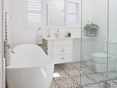 Modern white bathroom with freestanding bath, white shutters on window and large mosaic style floor tiles